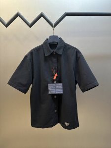 prada 徽标牛仔衬衫 定制臻绒高密幻影斜纹缎面料 以水洗单宁为画布 标志性prada三角标点缀于下摆 以prada复古铜扣轻叩现代美学 落肩剪裁勾勒慵懒廓形