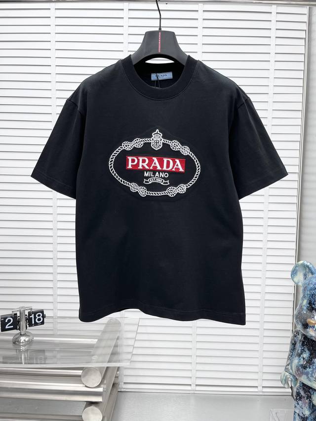 Prad*25Ss新品专柜同款胸前圆形立体绣花红色标字母三角标短袖T恤，这款T恤融运动风极简主义设计和精美细节于一身。拼接了进口家独家布料，前胸的Prada涂珐