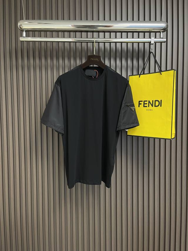 Prada 三角标嵌饰口袋短袖T恤，定制氦蚀丝光棱缎面料，标志性涂珐琅三角形金属徽标装饰衣袖，融合Re-Nylon尼龙织物点缀方正廓形，跨领域美学嫁接，精致的小