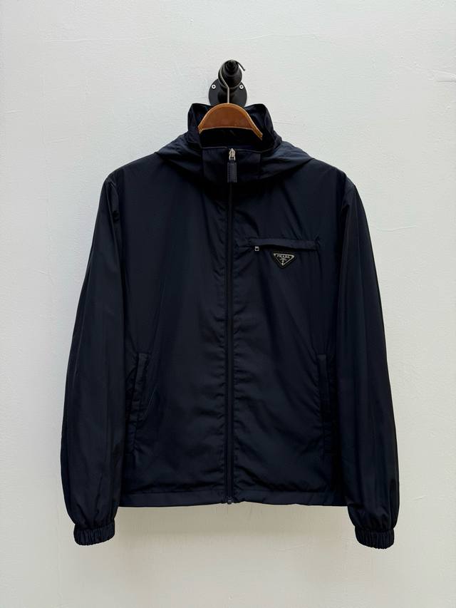 pr 高密度尼龙连帽外套 代工厂p出品 早春系列 胸前的金属三角徽标以几何极简形态为视觉锚点 既强化了品牌身份又避免过度装饰 拉链头和松紧扣上的品牌字样采用微雕