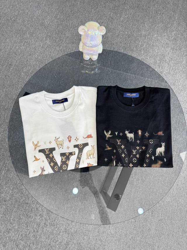 顶级版本 区别通货 25Ss路易威登夏季短袖 一个大写的黑色字母“V” 带有金色花卉图案。周围是各种卡通动物插图 采用有趣和异想天开的风格 散布着小星星 风格是