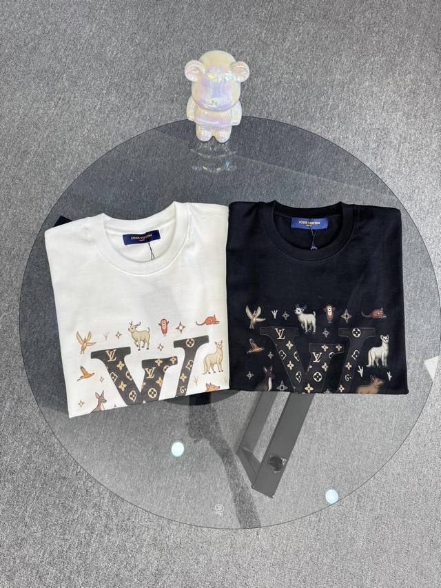 顶级版本 区别通货 25Ss路易威登夏季短袖 一个大写的黑色字母“V” 带有金色花卉图案。周围是各种卡通动物插图 采用有趣和异想天开的风格 散布着小星星 风格是