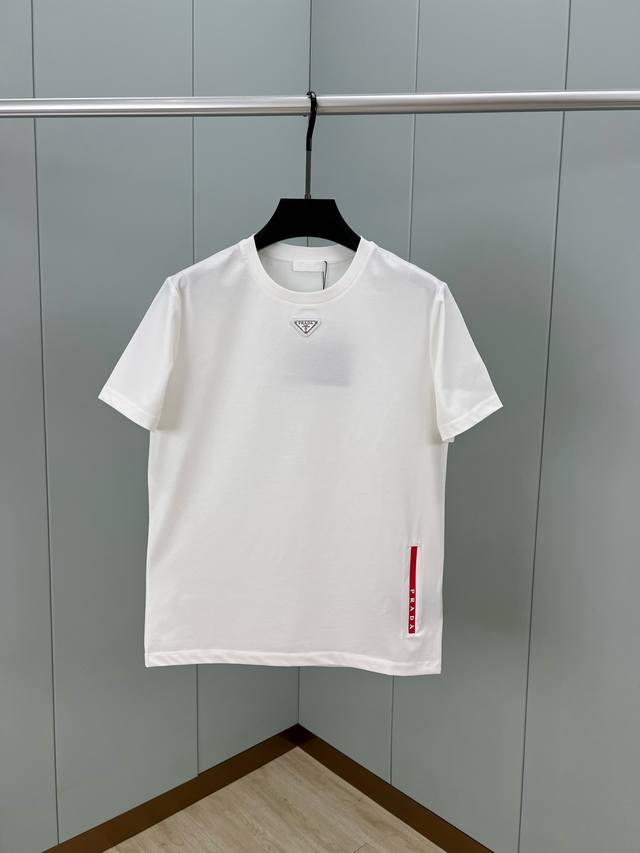 Prada.普拉达 春夏经典标志性的涂珐琅倒三角五金皮章短袖T恤，正面领口处下饰以品牌标志性的涂珐琅三角形金属徽标、左侧下摆处饰以品牌标识胶条徽标，凸显品牌辨识
