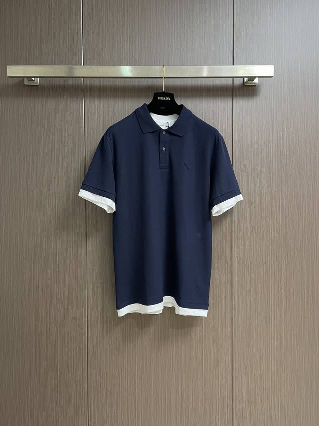 Prada 饰撞色织物三角标Polo衫，选用100％棉纤维编织而成的珠地布。棉纤维赋予面料吸湿透气，亲肤等特点。珠地结构表面呈现凹凸疏孔，形似蜂巢，促进空气循环
