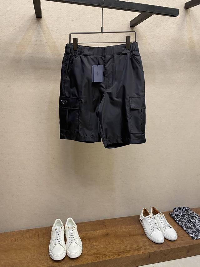 Prada、尼龙工装短裤 面料选择： 选用标志性尼龙面料制成，通过高密度的编织结构，使其具备高强度抗撕裂，耐磨性超群。经过表面纳米涂层处理之后使其具备一定的防水