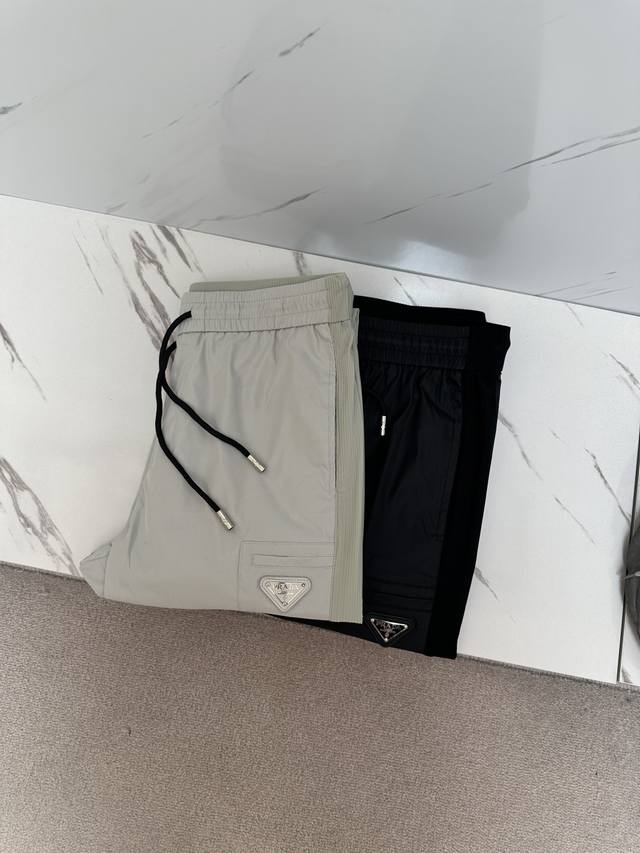 Prada 2025春夏新款休闲裤官网同步发售。定制品牌经典Logo，定制面料，舒适度极好，手触感强烈。辨识度极高，完美品相工艺。 尺码：M-3Xl