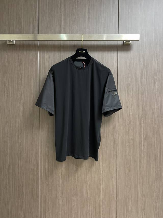 Prada 三角标嵌饰口袋短袖T恤，定制氦蚀丝光棱缎面料，标志性涂珐琅三角形金属徽标装饰衣袖，融合Re-Nylon尼龙织物点缀方正廓形，跨领域美学嫁接，精致的小
