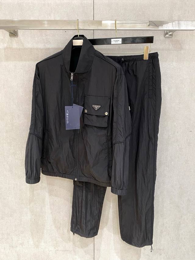 防晒服套装普拉达 上新25Ss早春运动套装 尼龙风衣卫裤 现货秒发 本款运动衫为轻盈科技面料全幅压印图案，注入动感气息，可与同款长裤共筑出行造型。进口原版Log