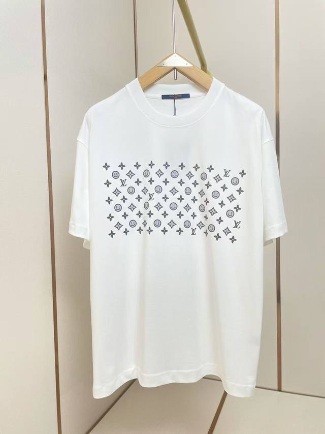 Lv 新款Cpfm笑脸T恤 T恤正面印有深色系重复图案组合：包含抽象笑脸符号、四叶草花纹以及品牌字母 T 的模块化排列，形成现代几何艺术效果 笑脸元素为日常穿搭