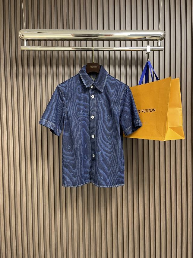 Lv 木纹短袖牛仔衬衫，本款短袖牛仔衬衫借由当季Lv Moire图案个性焕新，其间巧妙融入Monogram元素。同色印花映现丝绸般的莹润质感，珠光纽扣流露考究气
