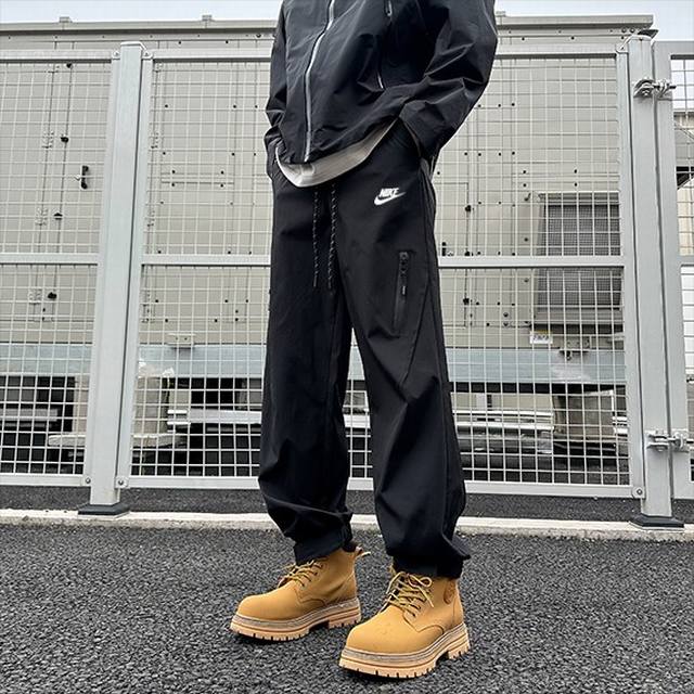 Nike 耐克 美式高街机能户外运动防水冲锋裤小脚休闲裤长裤 采用高科技防泼水面料，搭配美式高街工装设计，插兜处耐克印花Logo，裤腿处采用不规则拼接设计，搭配