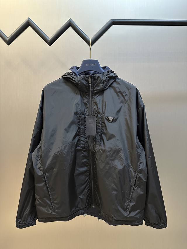 Prada 再生尼龙双面穿夹克风衣选用品牌标志性的再生尼龙面料，与传统尼龙性能相当，具备高强度，抗撕裂，耐磨损等特性。其质地轻盈，同时又具备防水功能适合多场景需