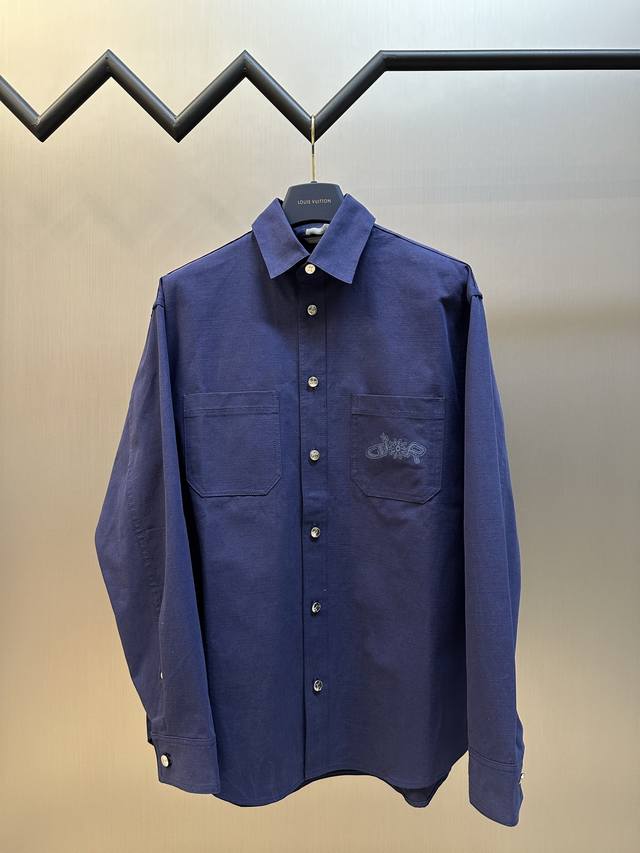 Dior Lewis Hamilton 谢幕衬衫采用蓝色棉质面料精心制作，胸前饰以贴袋，其中一个点缀以同色调联名系列刺绣，以图形风格重新诠释标志。可与该限定系列