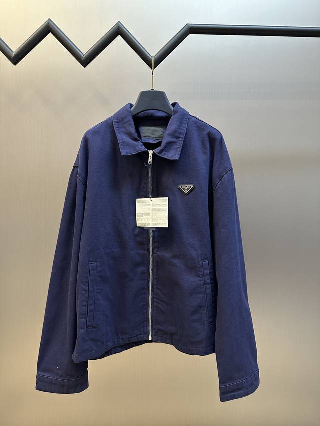 Prada 三角标做旧牛仔夹克定制纳米品蓝精纺牛仔布，以品蓝色为底色，标志性三角形徽标镶嵌在夹克之上，低调却极具辨识度。洗水复古做旧，通过特制溶液去除污渍且轻微