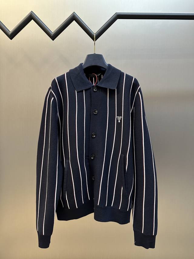 Prada 条纹刺绣长袖毛衣定织典藏级羊棉复合奢料，白色与红色条纹如灵动的音符，标志性Prada刺绣精致地镶嵌在毛衣之上。纽扣的排列与版型对称美感，在视觉上形成