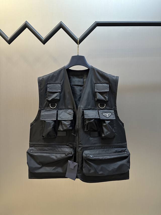Prada 工装尼龙马甲选用标志性尼龙面料制成，通过高密度的编织结构，使其具备高强度抗撕裂，耐磨性超群。经过表面纳米涂层处理之后使其具备一定的防水功能，又不失透