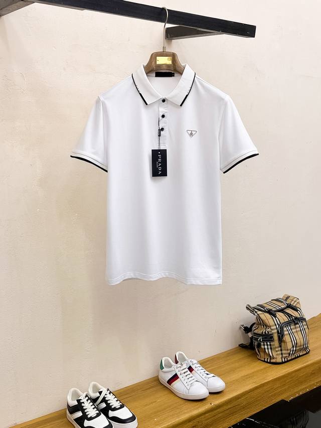 Prada 普拉达 2025 夏季新款男士翻领Polo衫，解锁意式优雅。领口设计是整件短袖的点睛之笔，简约线条勾勒出利落造型，标志性品牌Logo以精致的刺绣工艺