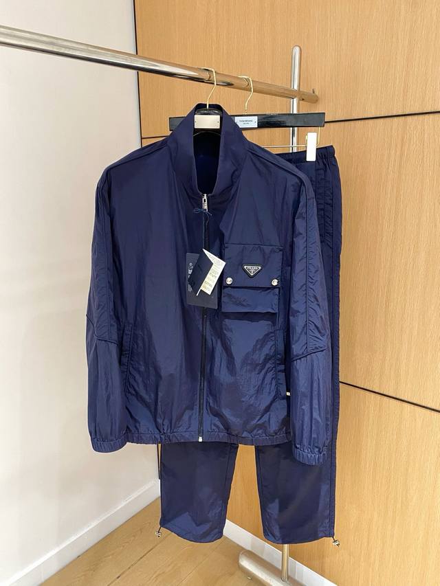 防晒服套装 普拉达 上新25Ss早春运动套装 尼龙风衣卫裤 现货秒发 本款运动衫为轻盈科技面料全幅压印图案，注入动感气息，可与同款长裤共筑出行造型。进口原版Lo