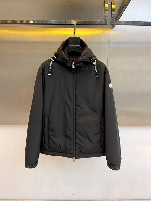 Mon蒙口、2025秋冬连帽棉服夹克外套。 Moncler黑色连帽羽绒服，以立体绗缝工艺勾勒雪域轮廓。肩带 Montcler 字样如登山者勋章，左袖圆形徽标烙印