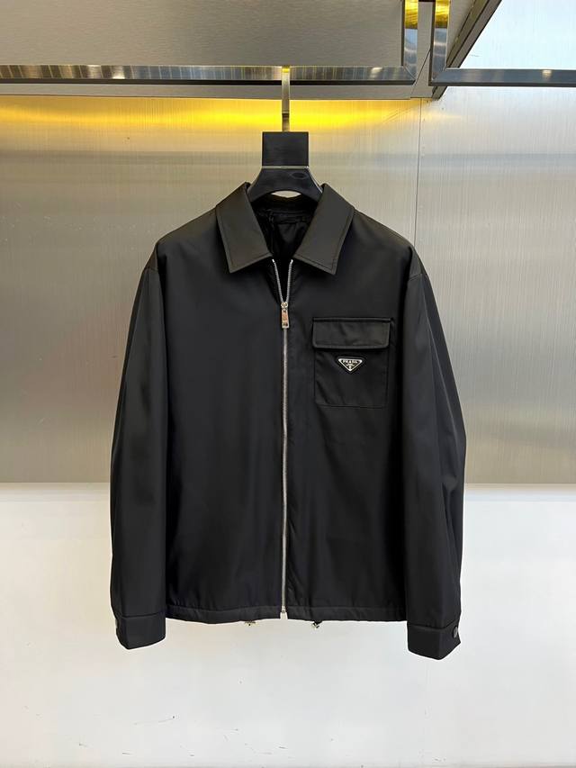 Prada 2025秋冬夹克。 高品质 这款Re-Nylon衬衫廓形简约流畅，融入运动细节，饰以涂珐琅三角形金属徽标。 Prada 2025秋冬系列黑色夹克，以
