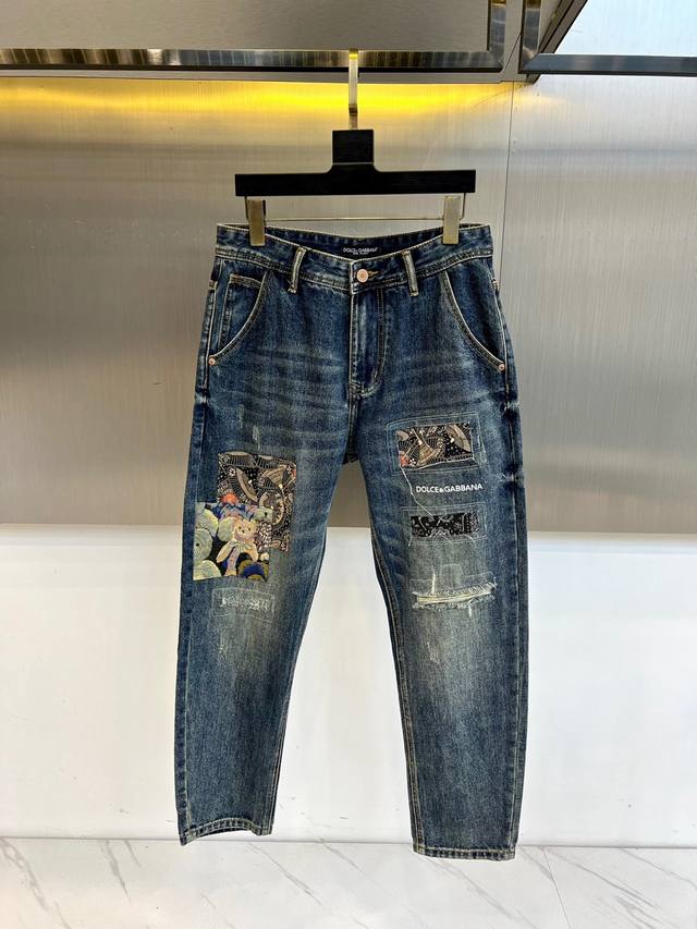 Dolce&Gabbana杜嘉班纳、2025秋冬新款牛仔裤，以经典蓝色丹宁为基底，水洗做旧工艺打造独特复古质感。裤身多处补丁装饰，将Dolce&Gabbana标