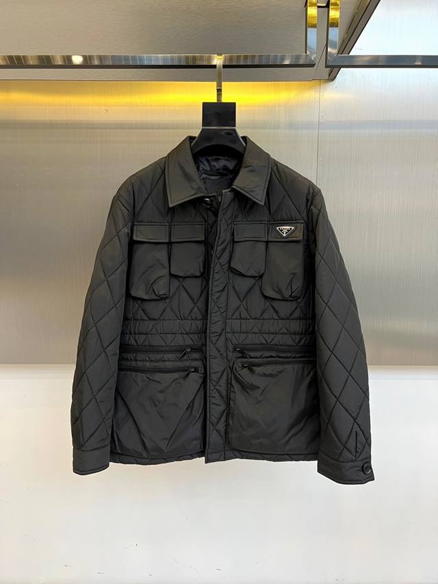 Prad普拉、25Fw秋冬新品黑色菱格纹翻领棉服夹克 通体黑色菱格绗缝如精密电路板，金属三角徽标在左胸划破沉寂 这是Prada留给都市暗夜者的身份芯片。对称翻盖