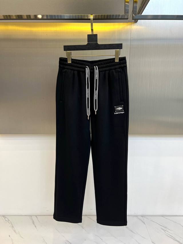 Balenciaga巴黎世家、2025秋冬新品男士束脚运动长裤，这款黑色长裤采用立体剪裁的束脚设计，腰部配备带有品牌标识的白色抽绳系统，裤腿侧边装饰黑色植绒标牌