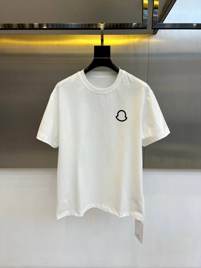 Mon蒙口、2025秋冬新品 极简圆领中袖打底衫。这款白色短袖T恤采用经典圆领设计与微阔版型，左胸处装饰品牌标志性的黑色抽象徽章图案，以极简线条展现现代美学。1