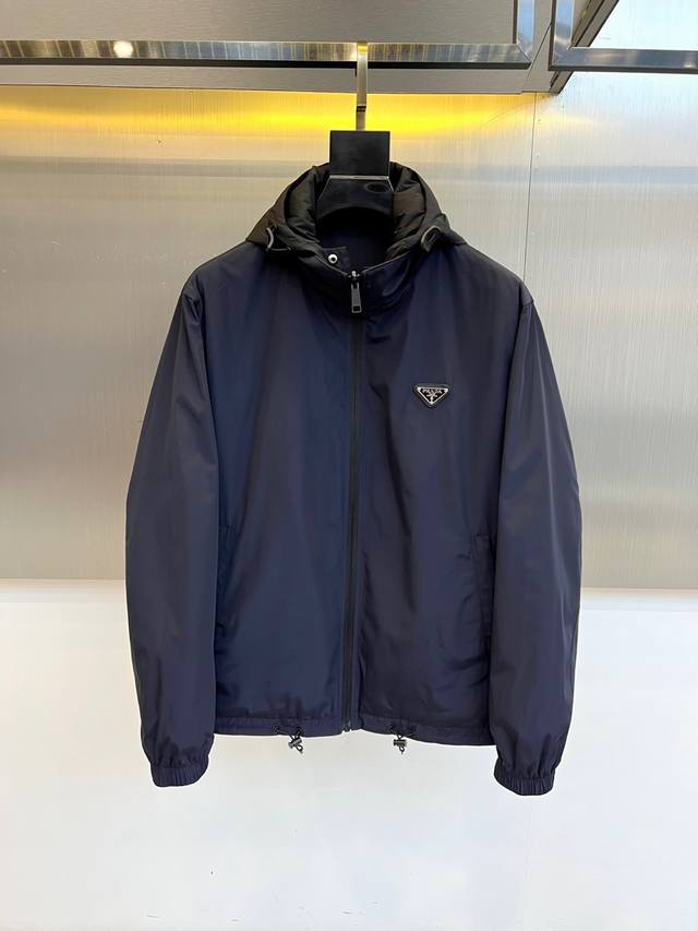 prad普拉、双面穿、2025秋冬新品深蓝色连帽夹克，以简约线条演绎现代都市美学。采用高科技尼龙面料打造立体廓形，连帽设计与顺滑拉链开合兼顾实用功能。左胸点缀标