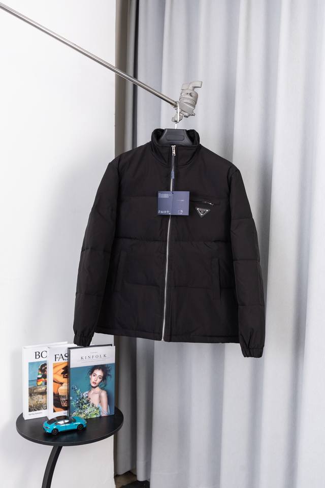 款号：S036 当普拉达的 “实用主义奢侈” 撞上冬日保暖刚需，这款立领棉服以标志性三角标与硬核御寒设计，成为高阶男士的暖冬风格密钥。前胸金属三角徽标，是普拉达