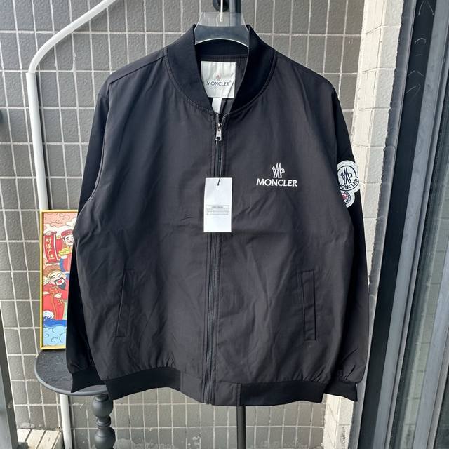 款号：Tt114 Mon蒙口、2025秋冬新品男士夹克，以高级灰色诠释都市机能美学。采用立领设计搭配顺滑拉链开合，左胸压印品牌标志性字母标识与徽标图案，右臂饰有