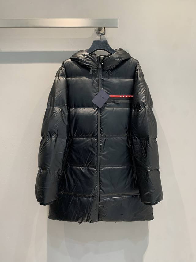 新款出货啦 Prad*2025秋冬新款红标连帽中长款羽绒服。黑色尼龙面料+90%白鸭绒填充，保暖又轻盈汁。防水压胶工艺，拼接处全封闭，防风防水超实用 码数Spl