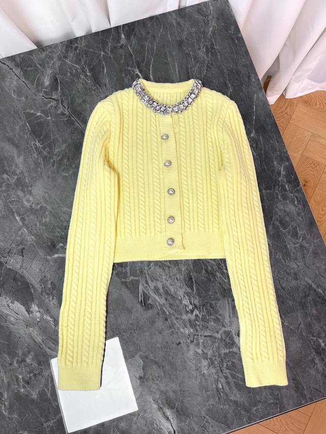 25新款 这款黄色针织开衫是一件极具设计感的单品 融合了经典针织工艺与华丽的装饰元素 它采用了精致的绞花针织纹理，呈现出细腻的立体效果 领口处镶嵌着闪亮的水晶装