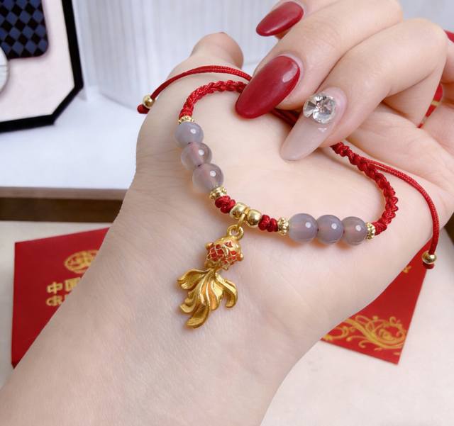 中国黄金锦鲤红绳年年有余手链新年限定 DDD 戴上它，把一整年的好运都圈在手腕间 DDD 红绳缠绕着通透的冰透镯身，像凝住了一汪清润的水。灰紫渐变的玛瑙珠串在腕